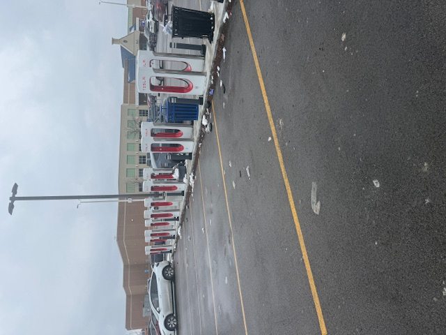 Existing EV charging site with wet pavement, scattered trash, and limited surrounding amenity support